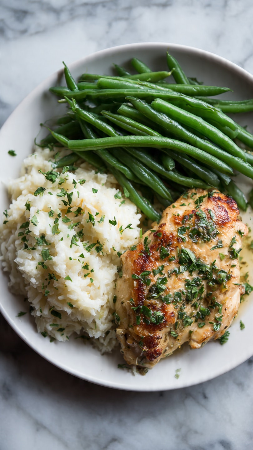 A white plate holds three main parts: a piece of cooked chicken with a golden brown and slightly crispy surface sprinkled with chopped green herbs on the right; a serving of white rice with a soft texture and some green herbs scattered on top placed in the bottom left; and fresh, bright green cooked green beans with a smooth, shiny surface arranged neatly in a cluster on the top left. The plate sits on a white marbled surface. photo taken with an iphone --ar 4:5 --v 7