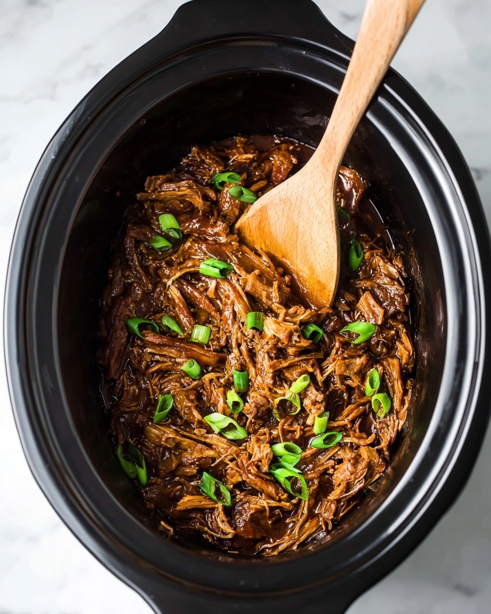 Inside a black slow cooker, there is one thick layer of shredded brown meat with a shiny texture, mixed well with a rich, dark sauce. On top, fresh green onion slices are scattered, adding bright green spots across the meat layer. A wooden spoon with a light brown smooth texture is placed in the slow cooker, partially buried in the meat, showing some sauce on it. The slow cooker sits on a white marbled surface. photo taken with an iphone --ar 4:5 --v 7
