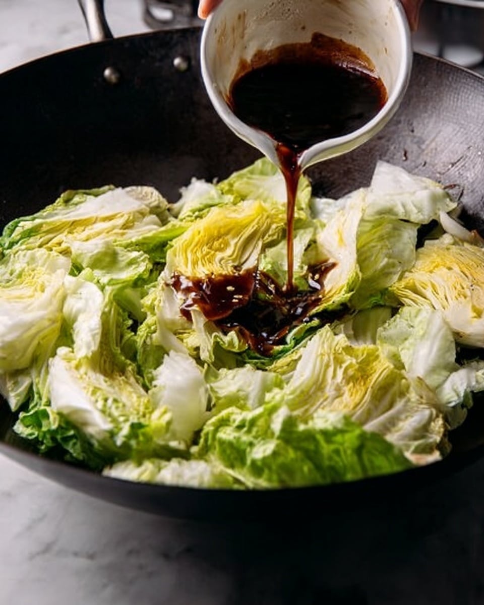 A large black wok is filled with several large, loose leaves of pale green and light yellow cabbage layered unevenly, some edges slightly wilted. Dark brown sauce is being poured slowly from a small white bowl held by a woman's hand above the center of the cabbage, creating a thick stream that drips onto the leaves. The surface under the wok is a white marbled texture. photo taken with an iphone --ar 4:5 --v 7