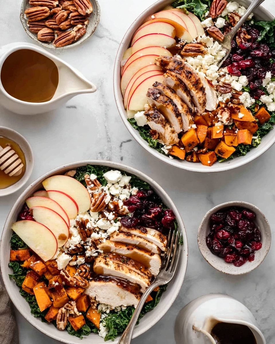 Two white bowls sit on a white marbled surface, each filled with several layers of food. The bottom layer is dark green kale with a rough texture. On top, there are slices of grilled chicken with a light brown, slightly charred surface. Thin red and yellow apple slices fan out on one side. Small cubes of bright orange roasted sweet potato are scattered across the bowl. White crumbles of cheese cover parts of the dish, adding a soft, crumbly texture. Dark red dried cranberries and whole pecans add more color and texture on top. A dark brown dressing is lightly drizzled over the layers. A silver fork rests inside one bowl. Nearby, there is a small white bowl with honey and a wooden honey dipper, a white jug with dark sauce, and small dishes of pecans, cheese, and dried cranberries. The photo taken with an iphone --ar 4:5 --v 7