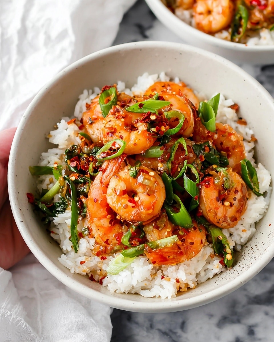 A black pan filled with several cooked shrimp that have an orange-pink color and shiny texture, mixed with green sliced scallions and small bits of black pepper, all covered in a glossy sauce. The shrimp are arranged closely together, showing their curved shape and a few slices of orange carrot peeking through. The pan sits on a white marbled surface. photo taken with an iphone --ar 4:5 --v 7