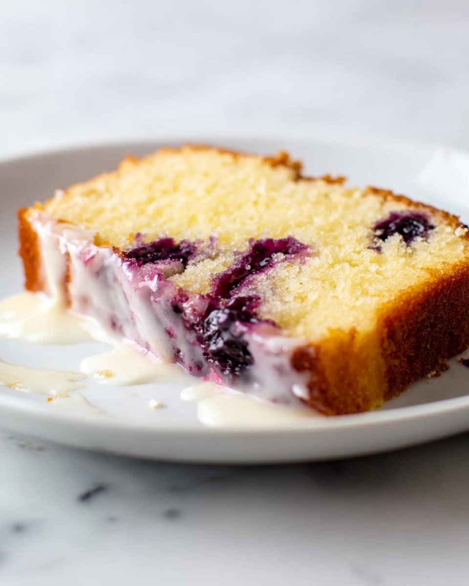 A thick slice of yellow cake with purple blueberries inside and on top, covered by a white icing layer, sits on a white plate. Behind the cake, there are two thin lemon slices placed vertically as decoration. The cake has a golden-brown crust and a soft texture. A few whole blueberries are also scattered around on a white marbled surface. The background is bright and plain white. photo taken with an iphone --ar 4:5 --v 7