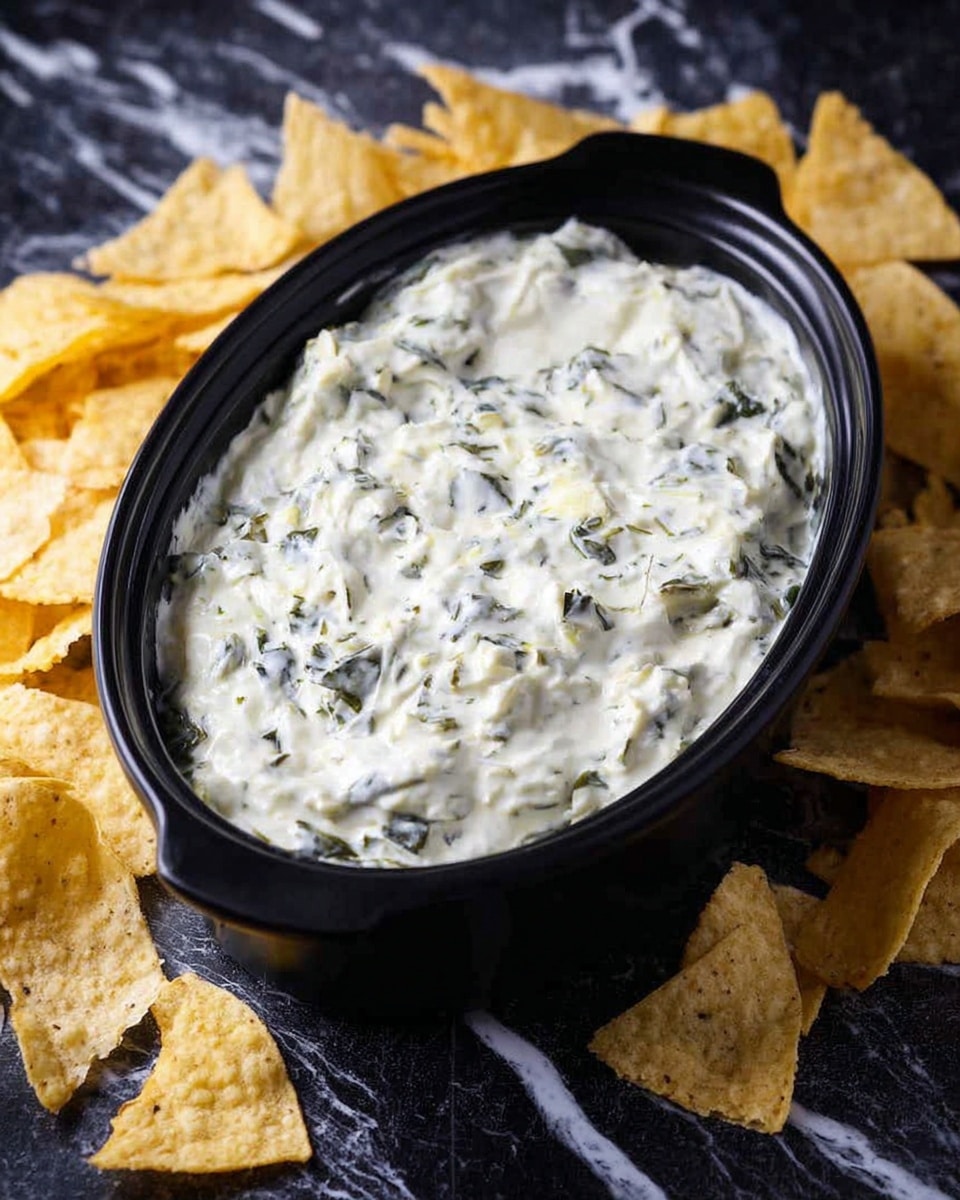 A black oval bowl filled with a creamy white dip that has small green leafy bits spread evenly throughout, showing a thick and slightly chunky texture. Around the bowl, broken yellowish tortilla chips are scattered on a dark surface. The background is changed to a white marbled texture. photo taken with an iphone --ar 4:5 --v 7