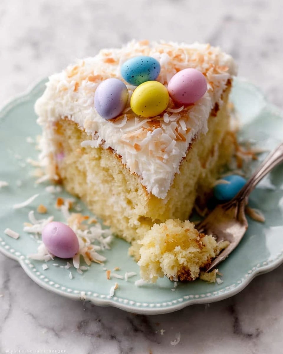 A slice of yellow cake sits on a white plate with scalloped edges, topped with a thick layer of white frosting and sprinkled with toasted shredded coconut. Mini pastel-colored candy eggs in blue, yellow, pink, and purple are placed on top and around the frosting, adding pops of soft color. The cake's texture looks moist and crumbly, with a small piece on a silver fork resting on the plate near the slice. The background is a white marbled surface. photo taken with an iphone --ar 4:5 --v 7