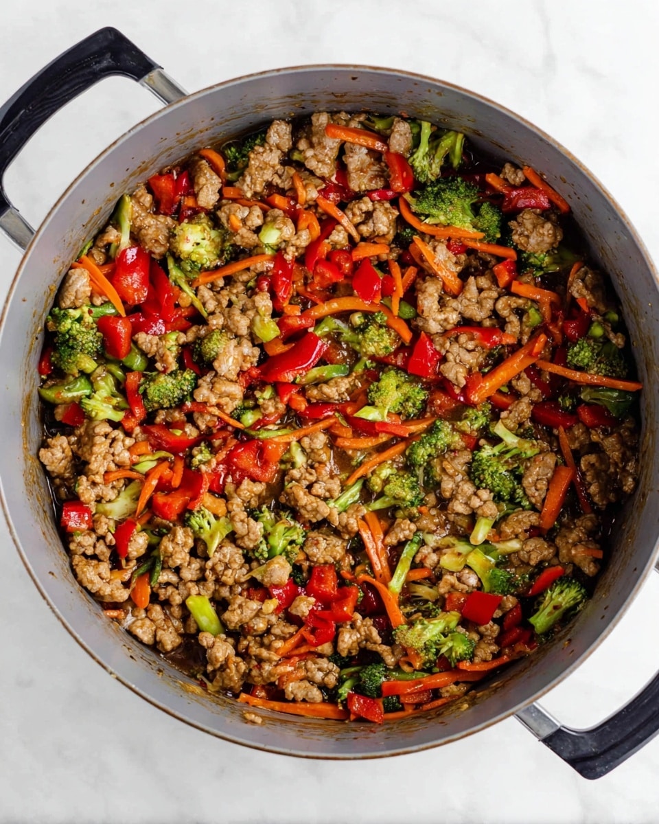The image shows a close-up view of a gray pot filled with a colorful stir-fry mixture. Inside, there are three main layers of ingredients: bright green chunks of broccoli, vivid red bell pepper pieces, and thin, orange carrot strips all mixed evenly with crumbled light brown cooked meat. The ingredients are coated in a glossy brown sauce that gives a slightly shiny texture. The pot has black handles on the sides, and the background is a white marbled texture. photo taken with an iphone --ar 4:5 --v 7