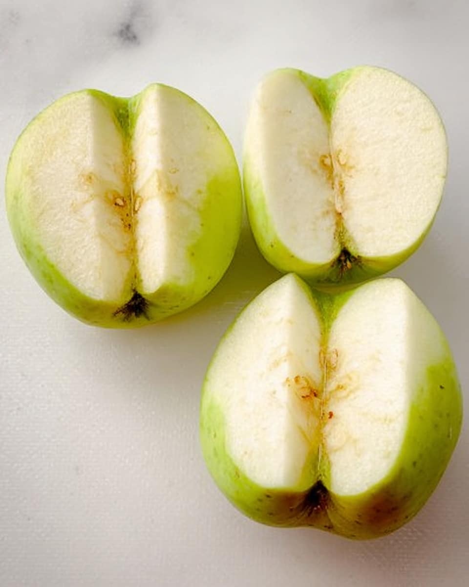 Two peeled green apples are sliced into four large pieces each. The apple segments show pale yellow flesh with some light brown spots and remaining green skin near the bottom. They are placed side by side on a white marbled surface. photo taken with an iphone --ar 4:5 --v 7