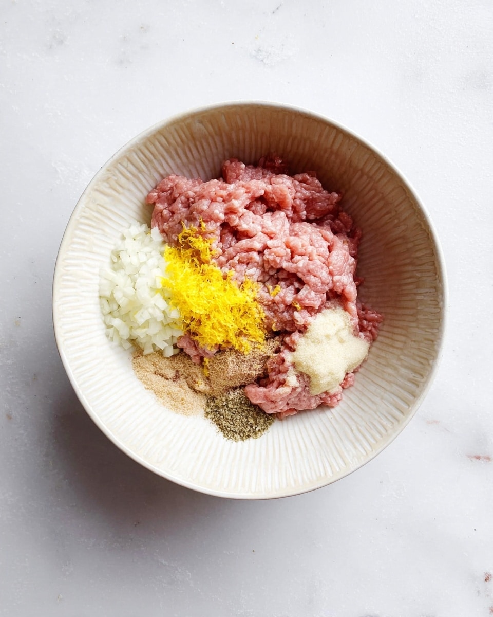 A white bowl with a textured rim sits on a white marbled surface filled with several layers of ingredients. At the bottom is a light pink raw minced meat layer. On top of the meat on one side, there is a bright yellow zest, likely from a lemon. Next to the zest, finely chopped white onion is placed in a small pile. There are small portions of light cream-colored minced garlic and fine brownish seasoning powders arranged neatly around the onion. The colors stand out clearly against each other, showing the separate layers before mixing. photo taken with an iphone --ar 4:5 --v 7