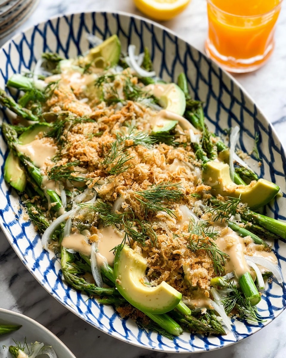 The dish is served on a white plate with blue zigzag patterns. The bottom layer consists of bright green asparagus spears spread evenly across the plate. On top of the asparagus are thin white onion slices scattered loosely. Next, there are thick slices of light green avocado placed in small groups. Over the avocado and onions, a creamy beige dressing is drizzled generously. The entire dish is sprinkled with a crunchy, golden-brown crumb topping. Small green dill sprigs are scattered across the dish for garnish. The plate is set on a white marbled surface with a lemon wedge and a glass of orange drink slightly visible in the background. photo taken with an iphone --ar 4:5 --v 7