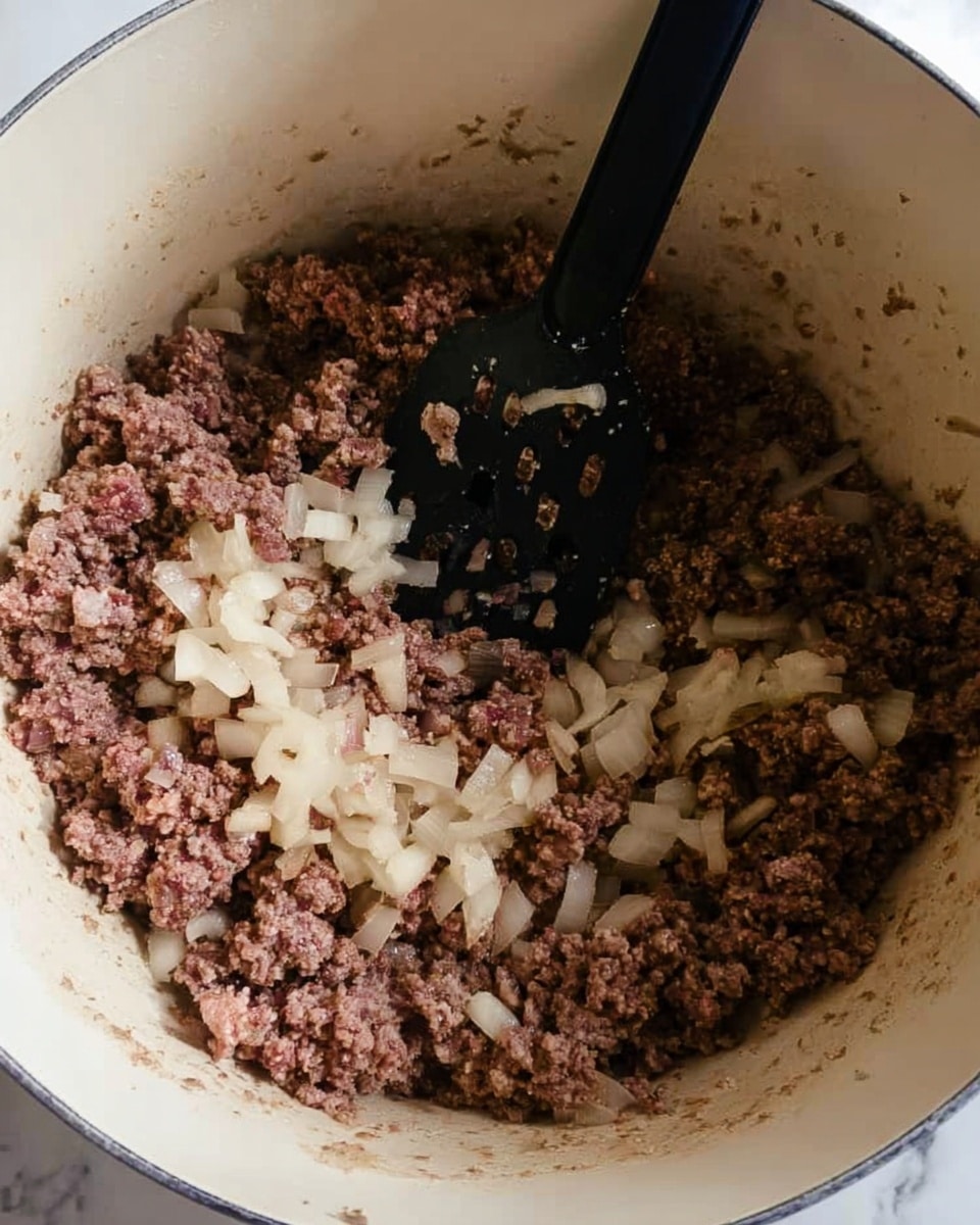Inside a white pot with light browning on the edges, there is a mix of chopped onions and browned ground meat being stirred by a black spatula with holes in it. The onions are translucent and pale, scattered evenly among the coarse, crumbly brown meat. The mixture fills the pot about halfway up, showing some steam or moisture. The photo has a close-up view from above showing the texture and color contrast well. The background is a white marbled surface photo taken with an iphone --ar 4:5 --v 7