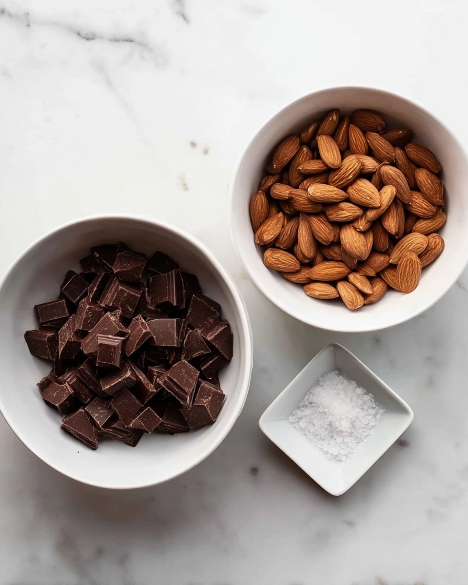 The image shows three white bowls placed on a white marbled surface. The large bowl on the left is filled with many small, dark brown square pieces of chocolate arranged in a loose pile. The large bowl on the right holds a pile of whole almonds with their smooth brown skins visible. In the center, there is a small white square bowl containing a small amount of white flaky salt. The overall look is clean and simple with natural colors. photo taken with an iphone --ar 4:5 --v 7