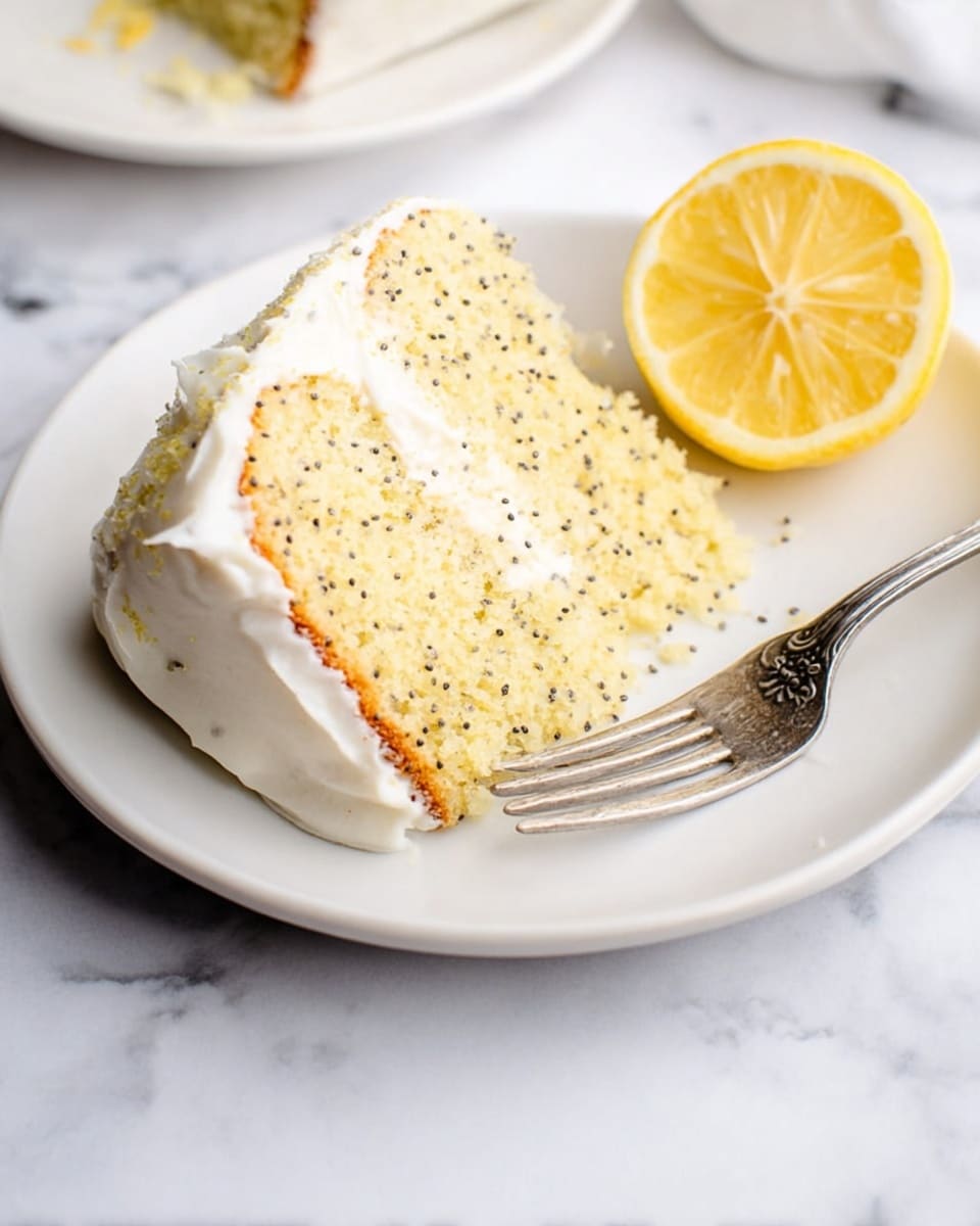 A slice of light yellow cake with small black seeds throughout, topped with a smooth white frosting layer. The cake slice sits on a white plate with a silver fork resting at the side. Next to the cake, there is a halved lemon showing its bright yellow inside. The whole scene is on a white marbled surface. Photo taken with an iphone --ar 4:5 --v 7