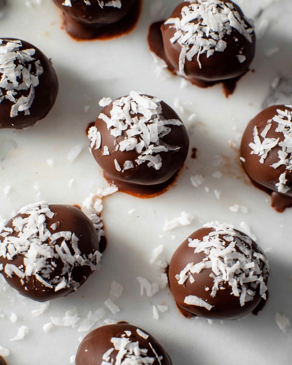 The image shows several round chocolate balls arranged on a white marbled surface. Each chocolate ball has a smooth, shiny, dark brown outer layer and is topped with scattered white coconut flakes that add rough, irregular texture. The chocolate coating looks thick and slightly imperfect at the edges, with small drips and smudges around the bases. The balls are spread out in a loose pattern, and the lighting highlights the glossiness of the chocolate and the softness of the coconut topping. photo taken with an iphone --ar 4:5 --v 7
