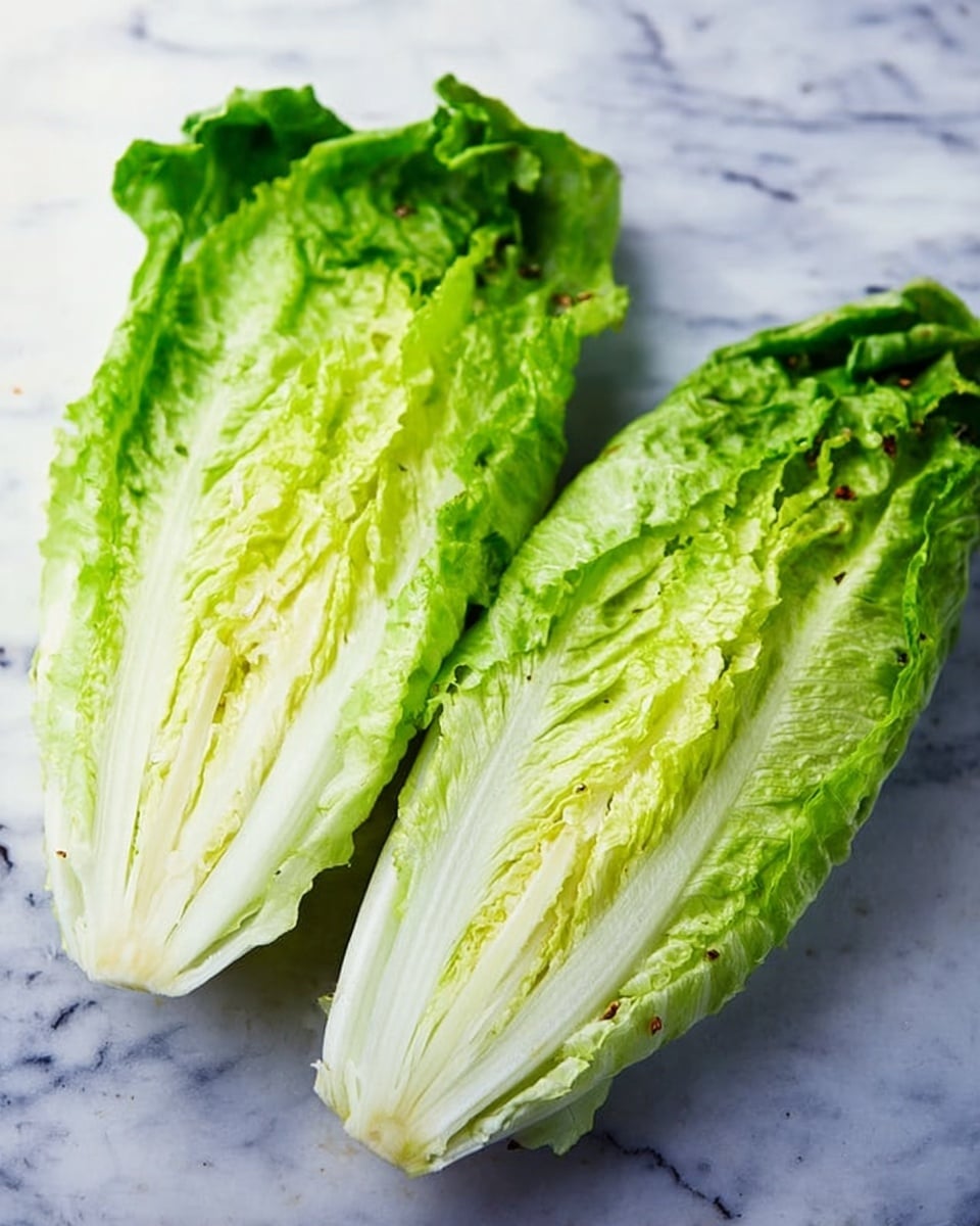 The image shows two halves of a fresh romaine lettuce placed on a surface with a white marbled texture. Each half displays multiple layers of crisp pale green to light yellow leaves, tightly packed towards the base and spreading apart as they extend outwards. The texture of the leaves is slightly ruffled along the edges and smooth near the center ribs. The bottom part is a thick white core, which transitions into the leafy layers above. The photo captures the freshness and natural texture of the lettuce clearly, photo taken with an iphone --ar 4:5 --v 7