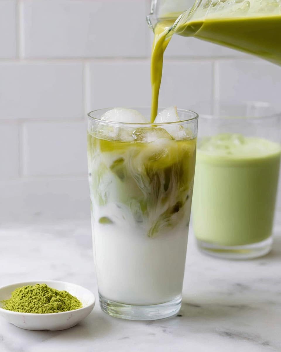 A clear glass in the center is filled with a bottom layer of white milk and ice, with a green tea liquid being poured in from above, swirling and mixing visibly with the milk to create a marbled effect. Behind and to the right of this glass is another clear glass filled with a smooth, light green matcha drink. On the left side of the image, there is a small white dish holding bright green matcha powder. All items are placed on a white marbled surface with a clean, white tiled background. Photo taken with an iphone --ar 4:5 --v 7