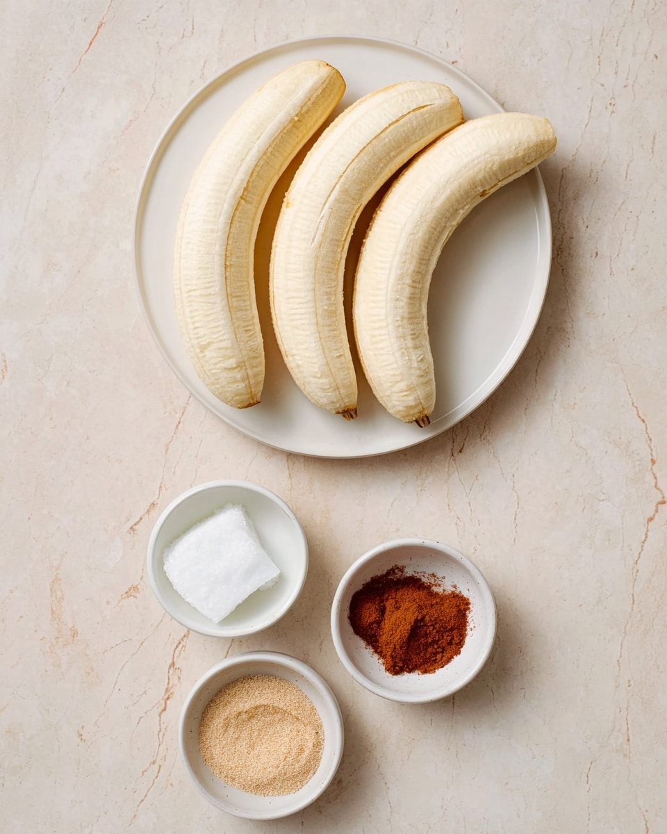 The image shows four peeled bananas placed side by side on a round white plate at the top. Below the plate, there are three small white bowls arranged in a vertical line on a white marbled surface. The top bowl holds a white, solid fat. The middle bowl contains a light brown granulated spice, and the bottom bowl has a fine reddish-brown powder. The background is simple and light, highlighting the colors and textures of the items photo taken with an iphone --ar 4:5 --v 7