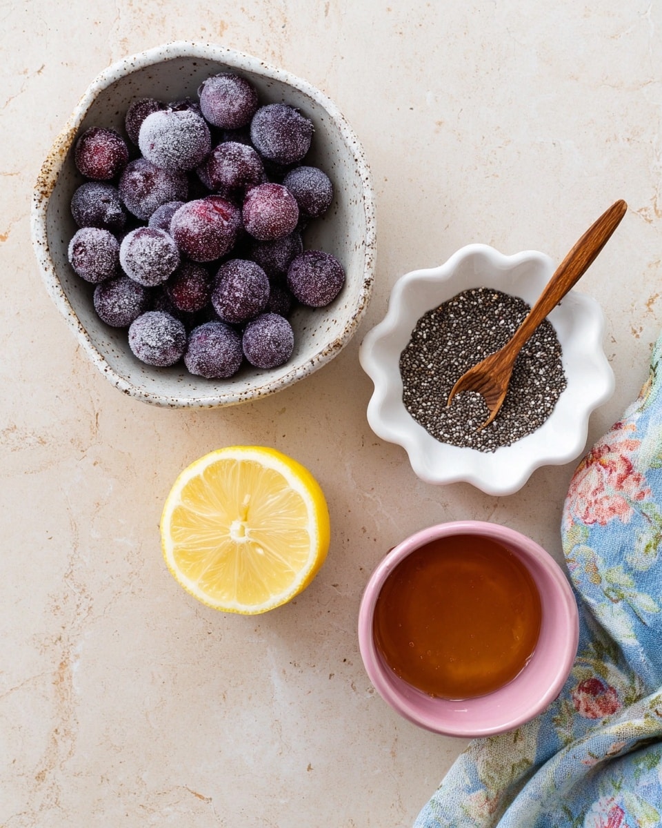 The image shows four main items arranged on a light beige surface with a floral cloth partly visible at the bottom right. At the top left, a speckled white ceramic bowl is filled with round, dark purple frozen berries covered lightly in frost. To the right, a small white scalloped bowl contains a mix of dark and light chia seeds, with a small wooden fork resting inside. Below the berry bowl, there is a bright yellow lemon half showing its juicy, segmented interior. Below the chia seeds bowl, there is a small pink ceramic cup filled with thick amber honey. The whole scene is bright and clear, with a soft natural light coming from above. Photo taken with an iphone --ar 4:5 --v 7