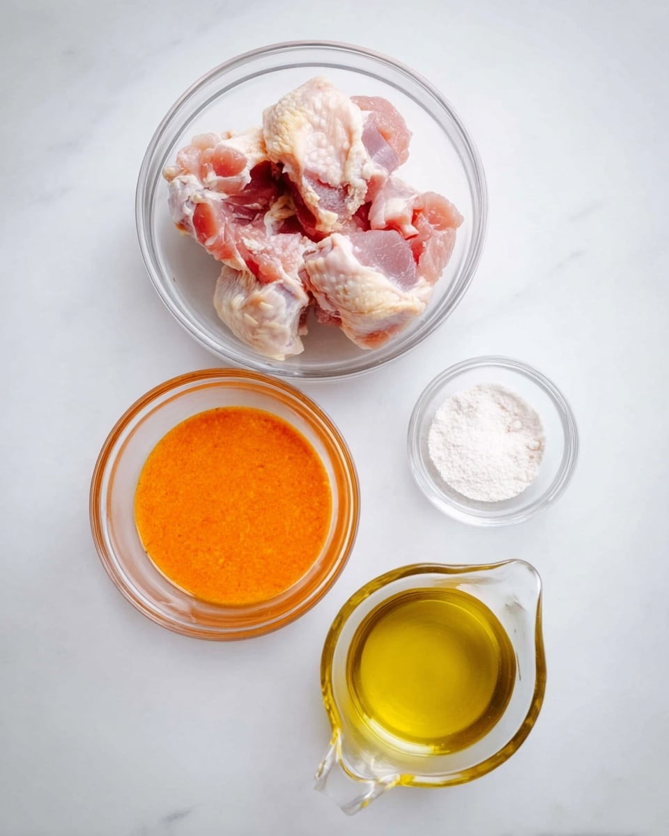 The image shows four clear glass bowls arranged on a white marbled surface. The largest bowl at the top contains raw chicken pieces which are pale with pinkish tones and some visible bone texture. Below it to the left is a medium-sized bowl filled with a smooth, bright orange sauce that looks thick. To the right of the sauce bowl is a small bowl holding white powder, likely salt or flour. At the bottom center is a clear glass container with a spout, filled with light yellow oil that has a shiny surface. Photo taken with an iphone --ar 4:5 --v 7