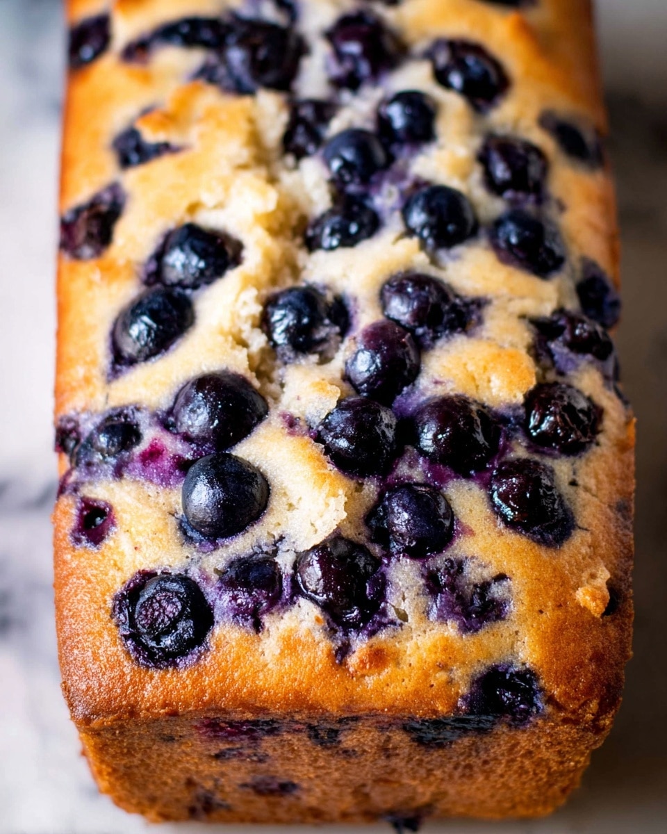 A close-up view of a loaf cake with one main layer of golden brown texture that looks soft and moist. The top layer is light golden with dark blueberries scattered throughout, some slightly sunken into the cake. White icing drips down the sides in thick streams, unevenly flowing down the front and pooling slightly at the bottom. The loaf sits on a wooden surface with a blurred white marbled background. photo taken with an iphone --ar 4:5 --v 7