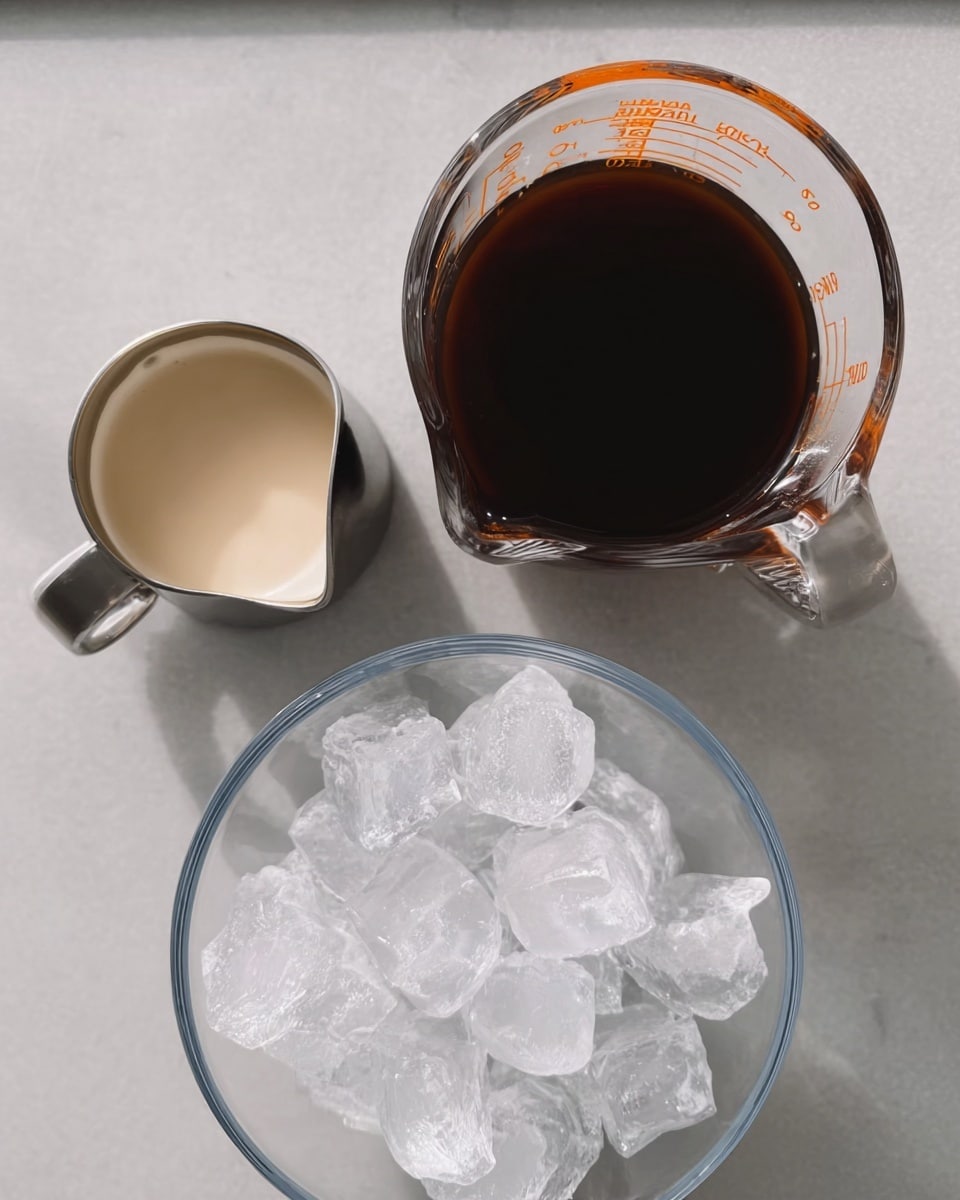 The image shows three small containers placed on a white marbled surface. At the bottom, there is a clear glass bowl full of large, clear ice cubes with a reflective texture. Above it, on the right side, is a glass measuring cup filled with dark brown liquid, likely coffee, with a smooth surface. To the left of the measuring cup, there is a small metal jug with a spout, filled with light beige cream. The items are neatly arranged with soft natural lighting, creating a clean and simple look. photo taken with an iphone --ar 4:5 --v 7