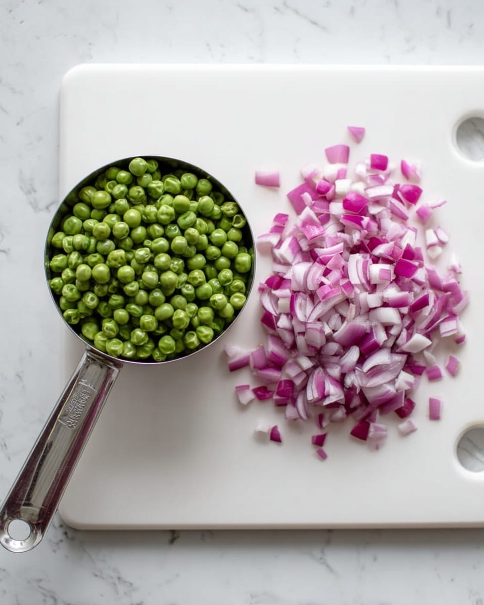 The image shows a white cutting board placed on a white marbled surface. On the left side of the board, there is a metal measuring cup filled with green peas, and on the right side, there is a small pile of chopped red onions with white and purple layers. The colors are fresh and bright, with the green peas and red onions creating a nice contrast against the white cutting board and marbled background. photo taken with an iphone --ar 4:5 --v 7
