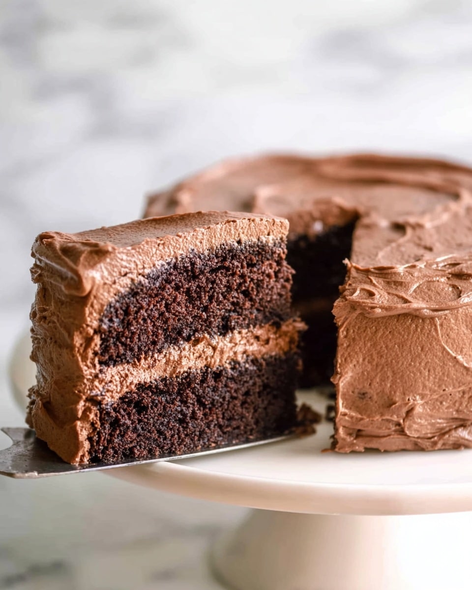 A close-up view of a two-layer chocolate cake slice on a white plate with a white marbled surface underneath, showing a thick layer of smooth light brown chocolate frosting between the dark brown soft cake layers. The top layer of the cake is covered with more rich chocolate frosting that looks creamy with slight ripples, and a silver fork is pulling up a small piece from the front of the slice, held by a woman's hand. Photo taken with an iphone --ar 4:5 --v 7
