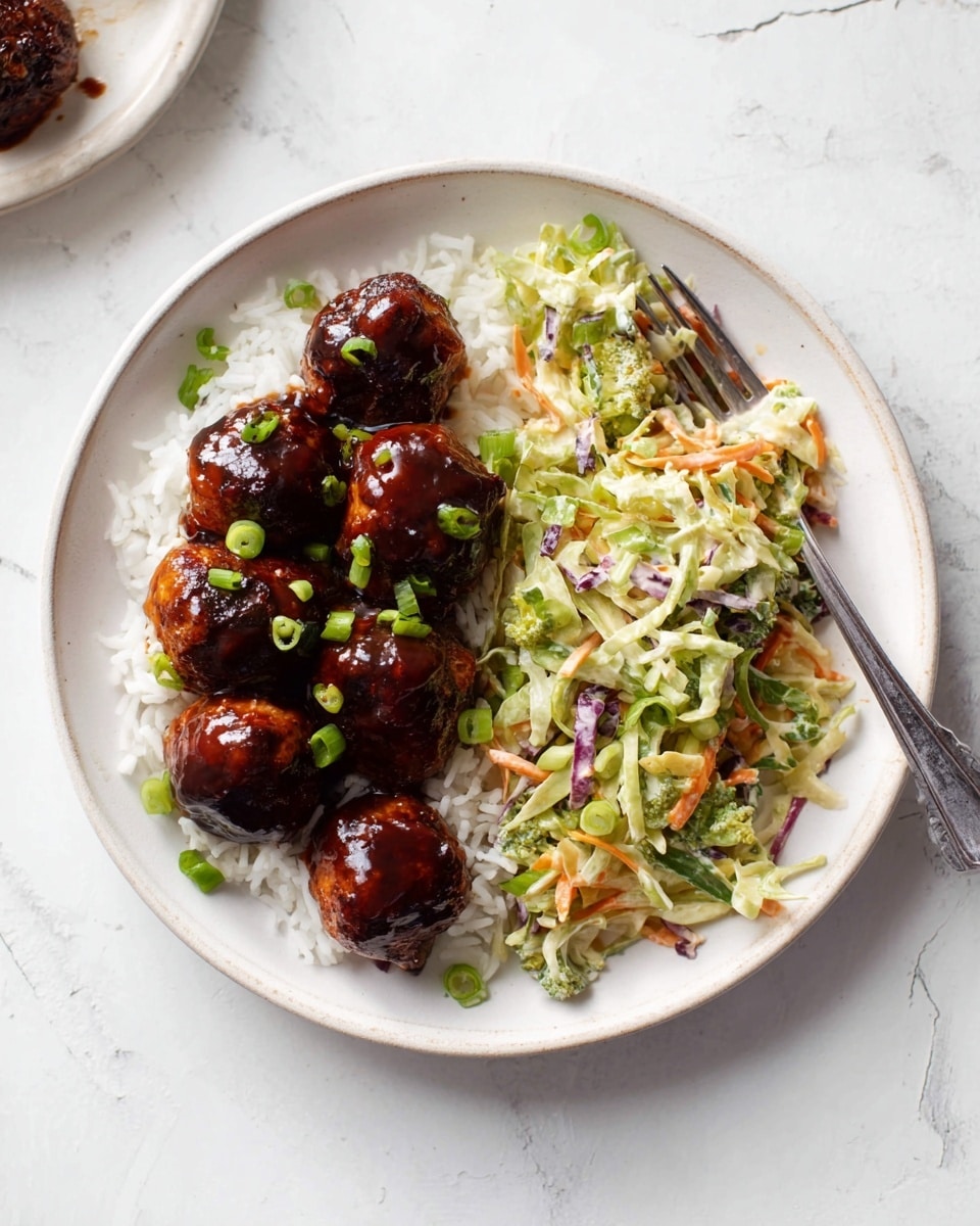 A white round plate on a white marbled surface holds a meal with three main parts: a base layer of white rice at the bottom left, topped with five shiny brown meatballs covered in dark sauce scattered with small green onion pieces, and a colorful slaw on the right side made of shredded light green broccoli stems, orange carrots, and some purple cabbage, all mixed with a creamy dressing and sprinkled with green onion slices. A silver fork rests on the plate's right side, partially in the slaw. Photo taken with an iphone --ar 4:5 --v 7